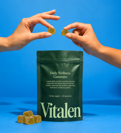 Two hands passing gummies over a Vitalen pouch on a blue backdrop