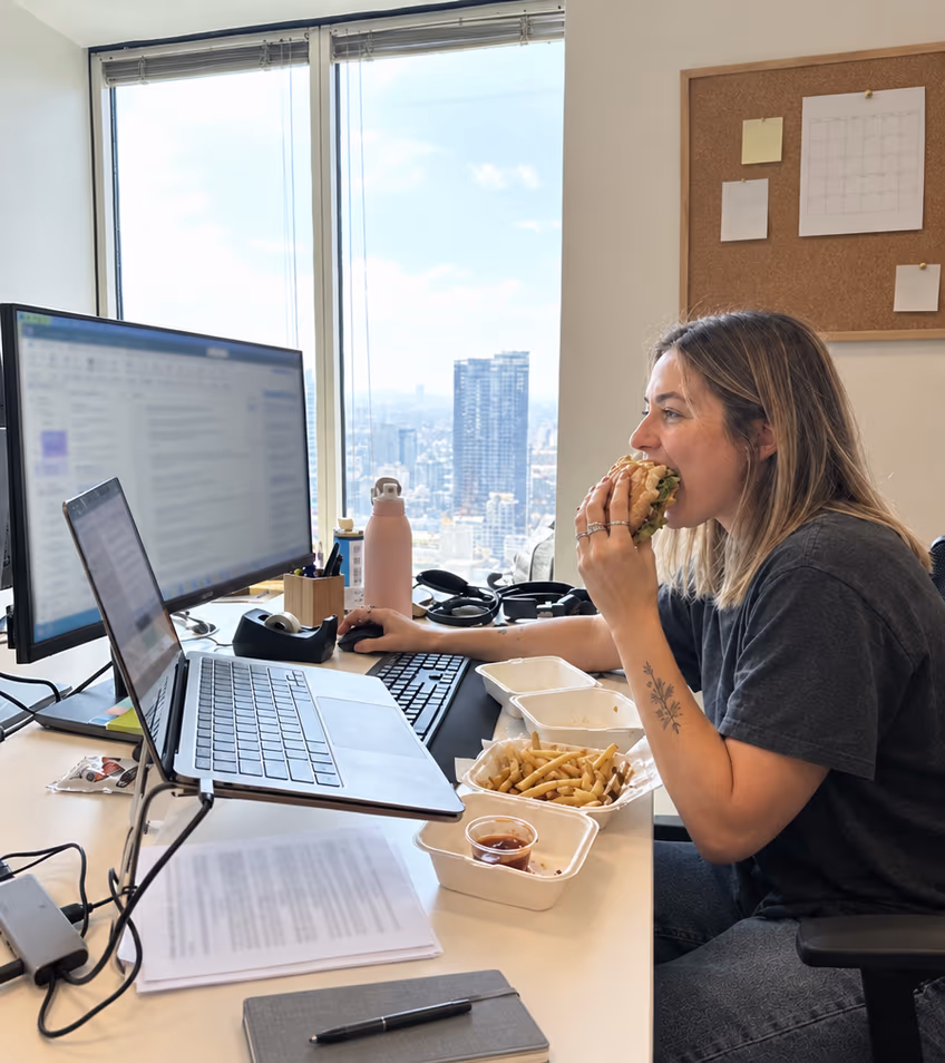 A woman eating a burger at her office desk while she keeps working