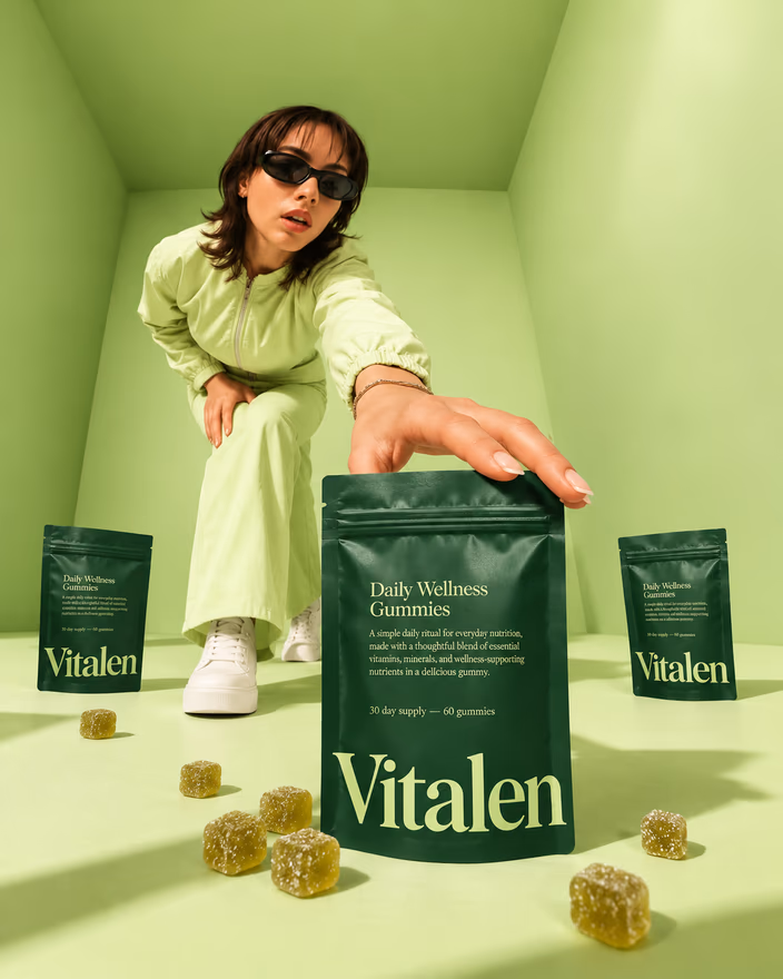 A woman in sunglasses reaching for a Vitalen pouch in a green room scattered with gummies